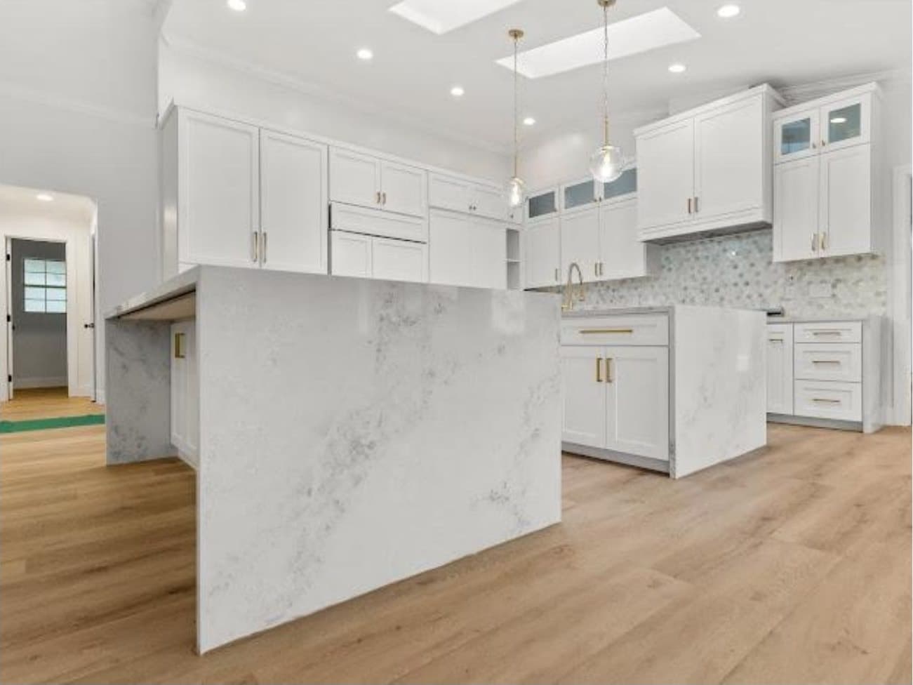 El Cajon kitchen waterfall island detail: quartz slab anchored center, pendant and skylight column rising behind, brass pulls on white shaker cabinets.